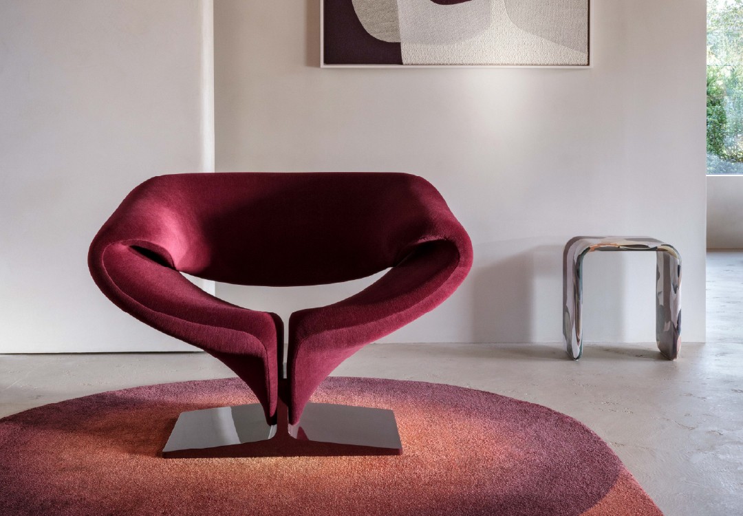 Sculpturale Ribbon fauteuil van Artifort in bordeauxrood, geplaatst op een rond kleed met warme tinten.