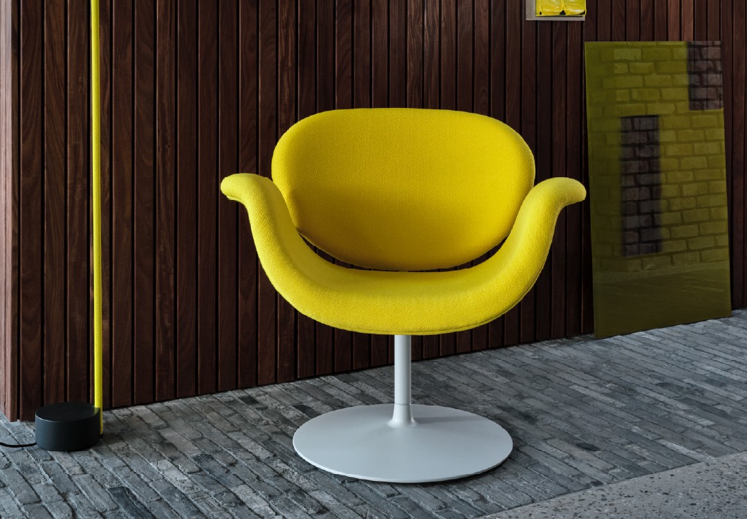 Gele Artifort Tulip fauteuil met witte voet, gefotografeerd vanuit een iets andere hoek tegen houten wand.