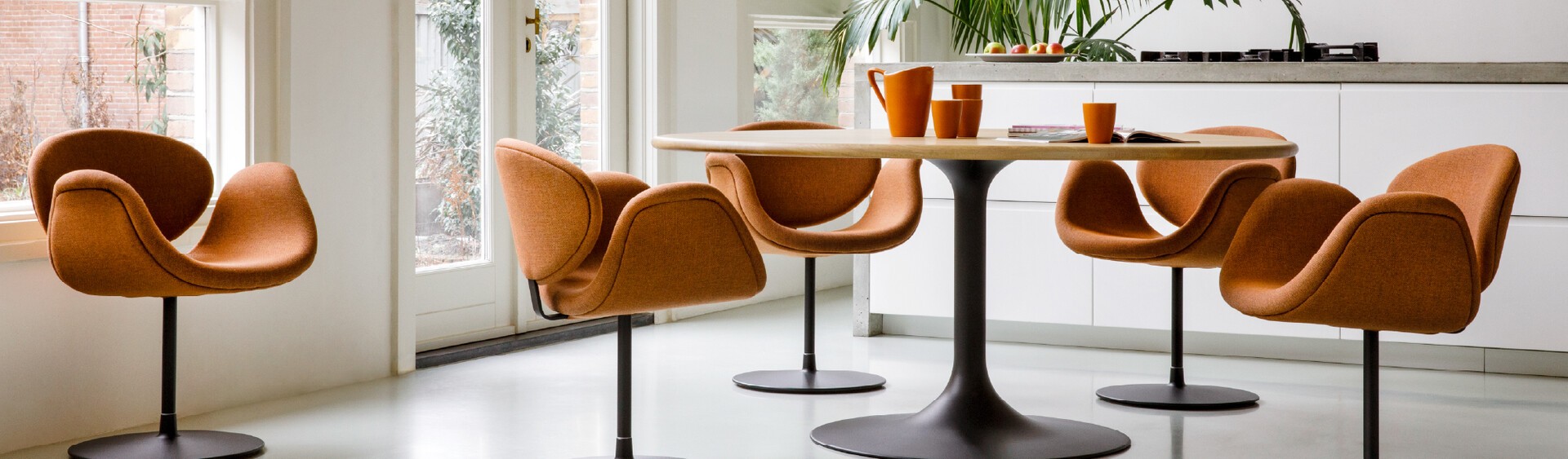 Vijf oranje Artifort Little Tulip stoelen rond een ronde eettafel in een lichte, moderne eetruimte.