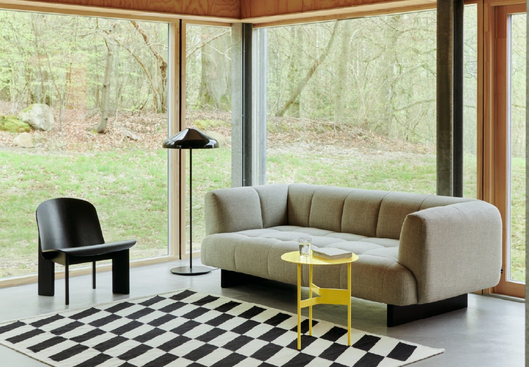 Grijze bank met gele bijzettafel Strak modern interieur met lichtgrijze geknoopte sofa, kleine gele bijzettafel met glas water en zwart vloerlamp voor een serene uitstraling