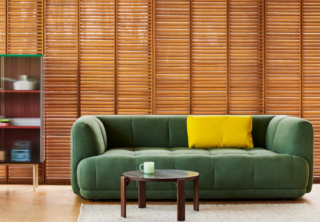 Woonkamer met groene bank en gele accenten Strakke, moderne woonkamer met donkergroene gestoffeerde sofa, heldergeel kussen, houten jaloezieën en een ronde, donkere salontafel
