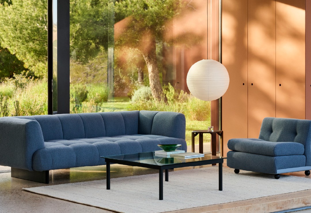 Modulaire blauwe sofa in lichte ruimte Ruime living met grote glasramen, blauw gestoffeerde modulaire sofa, glazen salontafel en hangende papieren lamp voor een frisse, luchtige sfeer