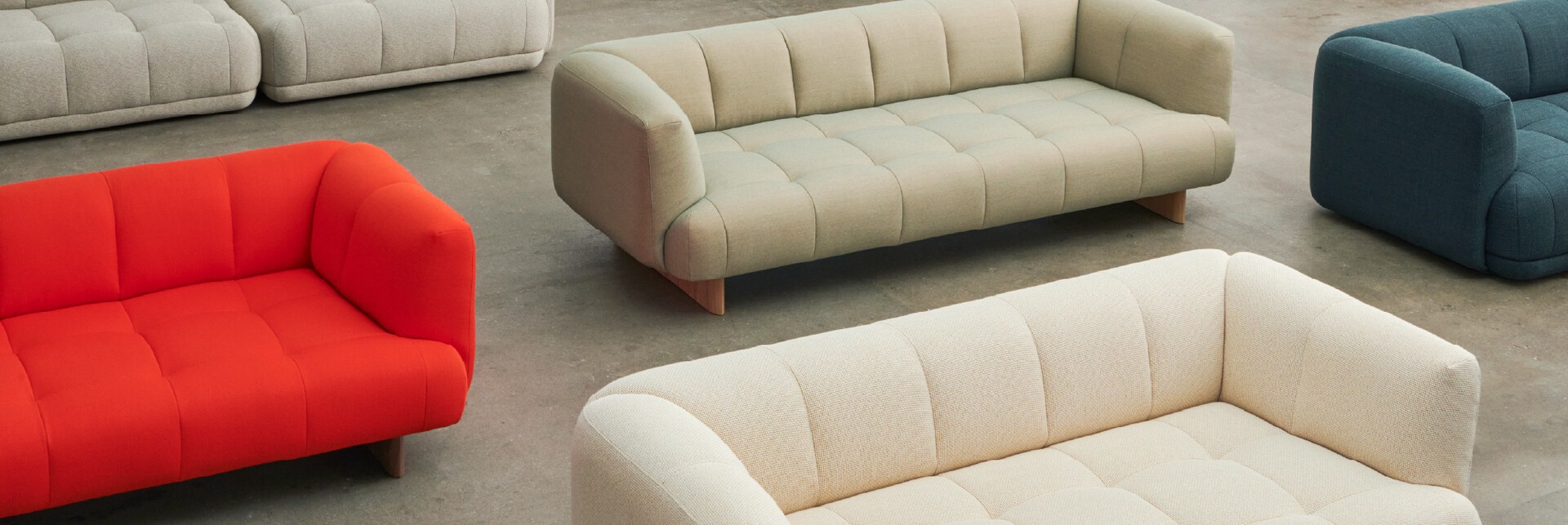 Gekleurde gestoffeerde banken Vijf gestoffeerde, geknoopte sofa’s in rood, beige, lichtgroen, donkerblauw en off-white op een strakke betonnen vloer voor productpresentatie