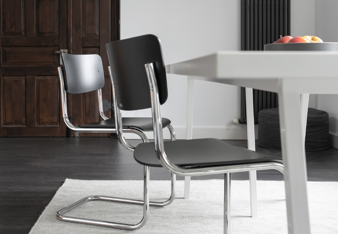 Thonet S43 stoelen met zwarte houten zitting en verchroomd buisframe rond witte tafel met fruitschaal in moderne eetkamer &ndash; Van Til Interieur.